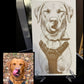 A custom engraved dog portrait print displayed on a stand, featuring a brown sketch of a dog wearing a harness on a white background, with a small inset photo of the real dog wearing the matching harness in the lower-left corner.